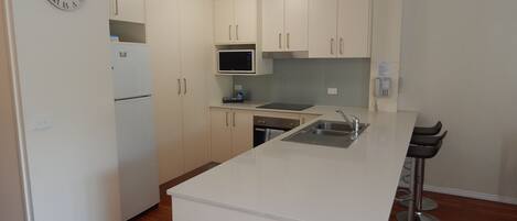 A compact kitchen with white cabinets, a built-in microwave, a refrigerator, a sink, and a bar stool.