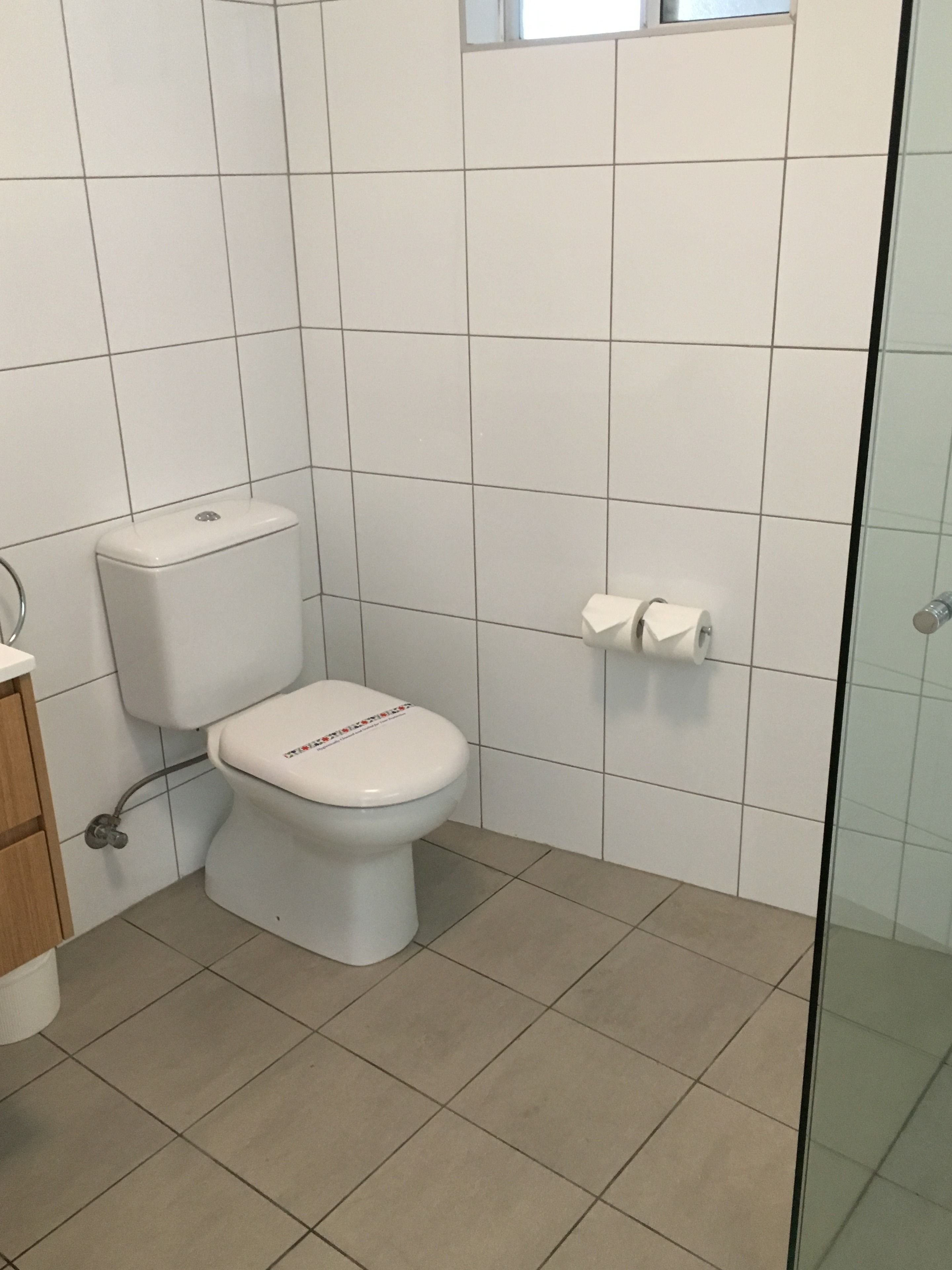 A bathroom with a toilet, a paper towel dispenser, and a glass shower enclosure.
