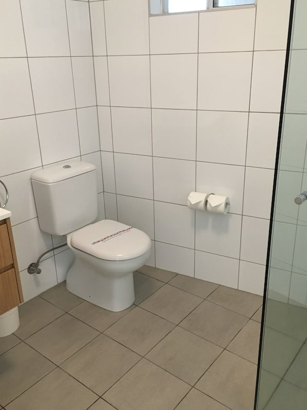 A bathroom with a toilet, a paper towel dispenser, and a glass shower enclosure. - Ocean Front at The Entrance (The Entrance)