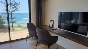A modern room with a large TV, two chairs, a desk, and a view of the ocean. - Ocean Front at The Entrance (The Entrance)