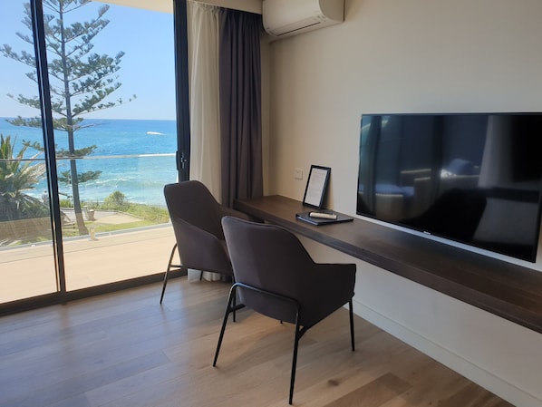 Una habitación moderna con una televisión grande, dos sillas, un escritorio y vista al océano.