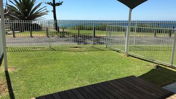 Ein überdachter Außenbereich mit Holzterrasse, einem eingezäunten Garten und Meerblick.