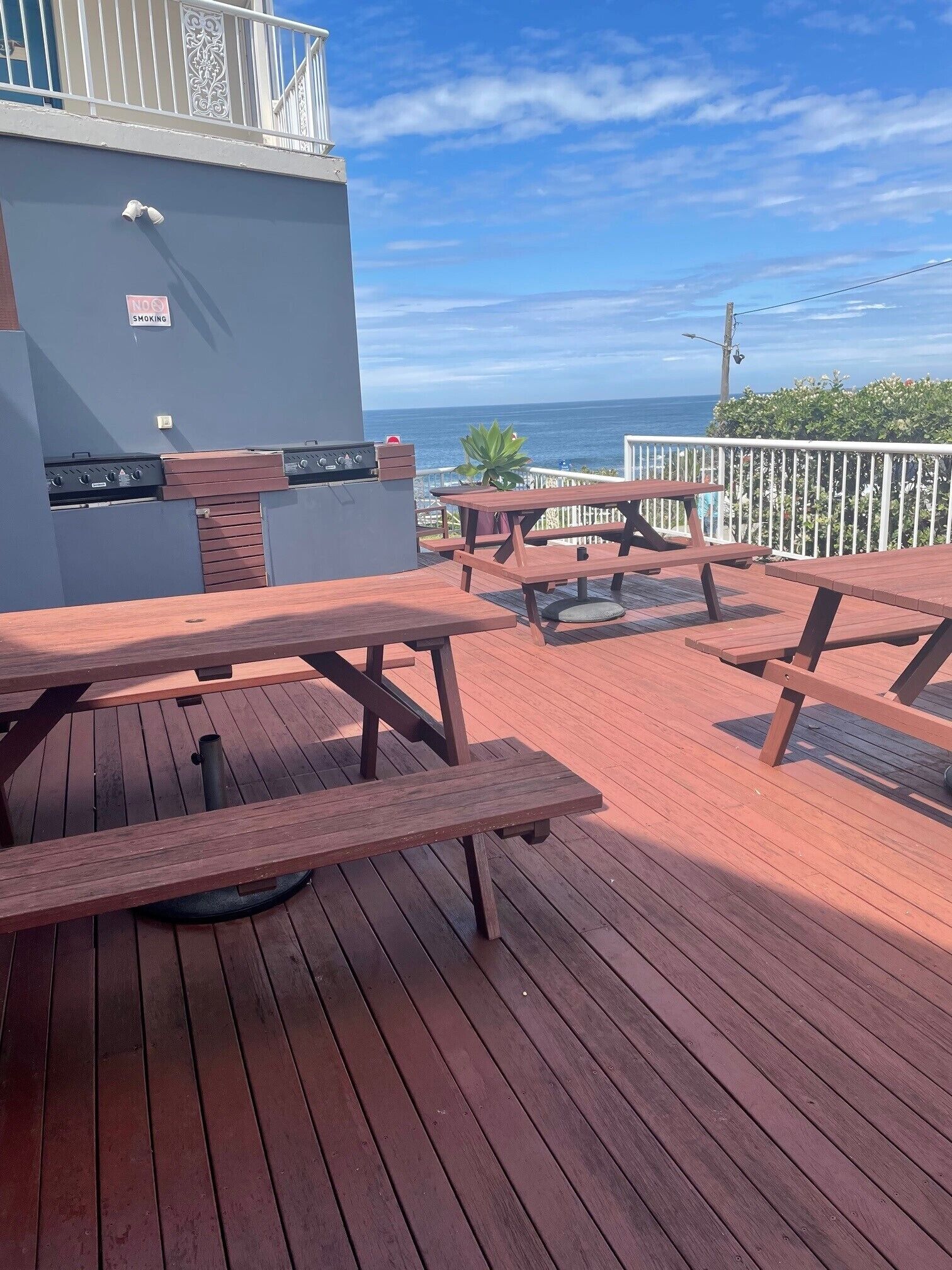 A wooden deck with picnic tables and a barbecue grill, overlooking a scenic ocean view.