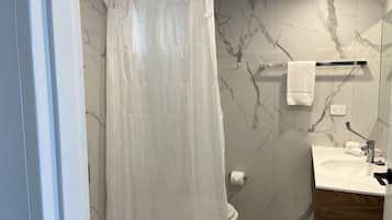 Une salle de bain avec un mur en marbre, des toilettes, un lavabo avec un meuble en bois et un rideau de douche.