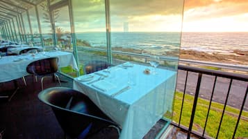 Un restaurant dont les tables sont dressées pour le service, offrant une vue sur la côte.