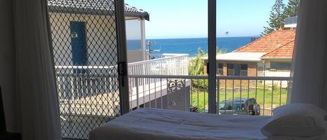 Een hotelkamer met twee bedden, een balkon met uitzicht op zee en een schuifglazen deur.