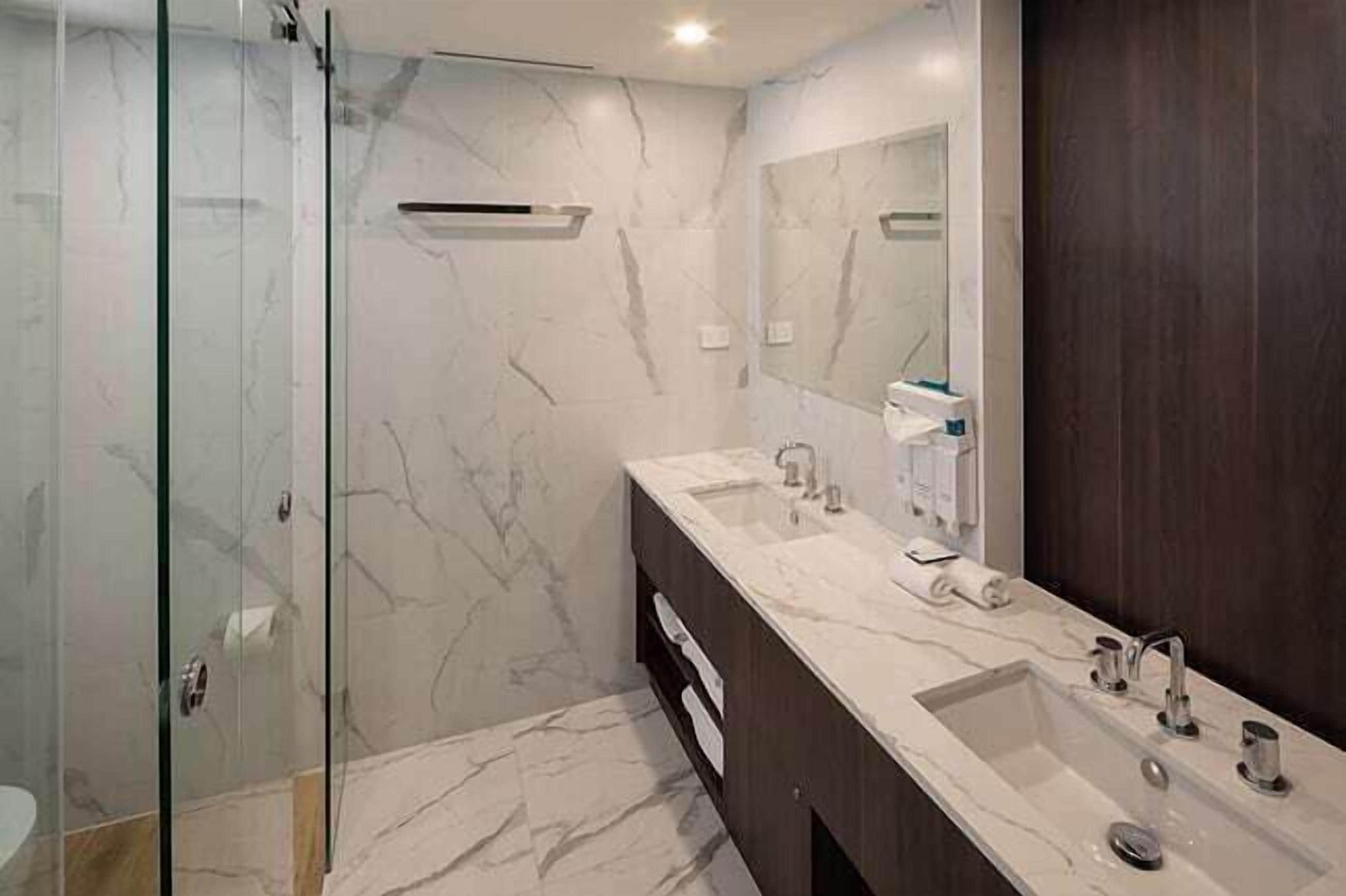 A modern bathroom with a glass shower enclosure, a dark wooden vanity, and a large mirror.