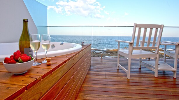 A wooden deck with a white chair and a bottle of wine, a bowl of strawberries, and two glasses of white wine. - Ocean Front at The Entrance (The Entrance)