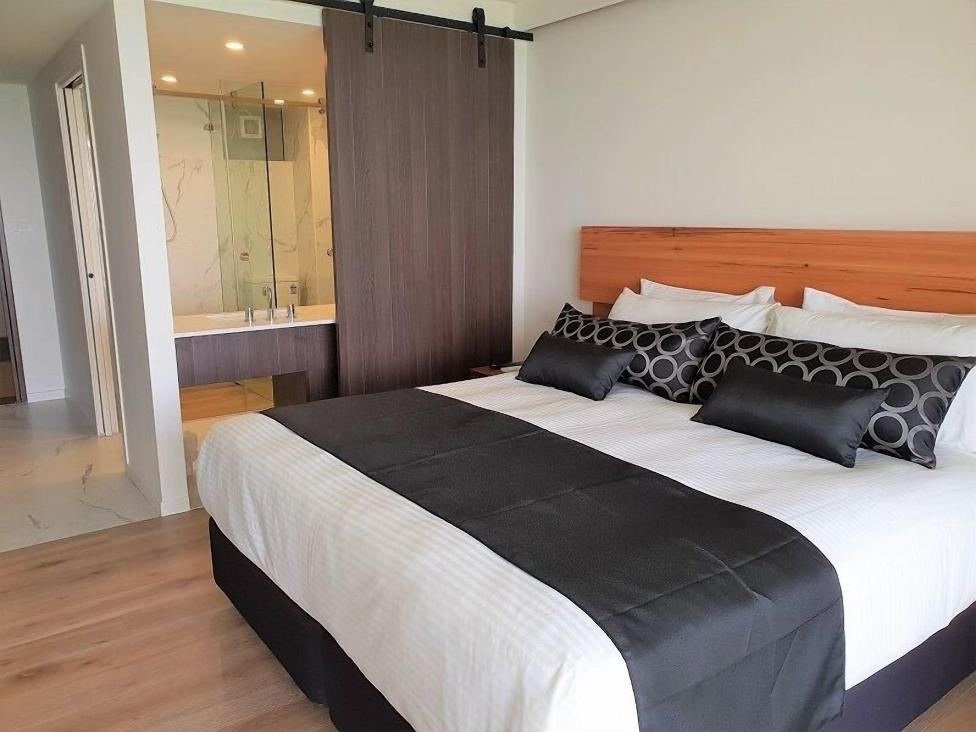 Un dormitorio moderno con una cama grande, cabecera de madera y un baño visible a través de una puerta corrediza.