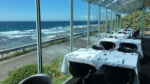 A restaurant with tables set for dining, overlooking a rocky coastline with waves crashing against the shore. - Ocean Front at The Entrance (The Entrance)