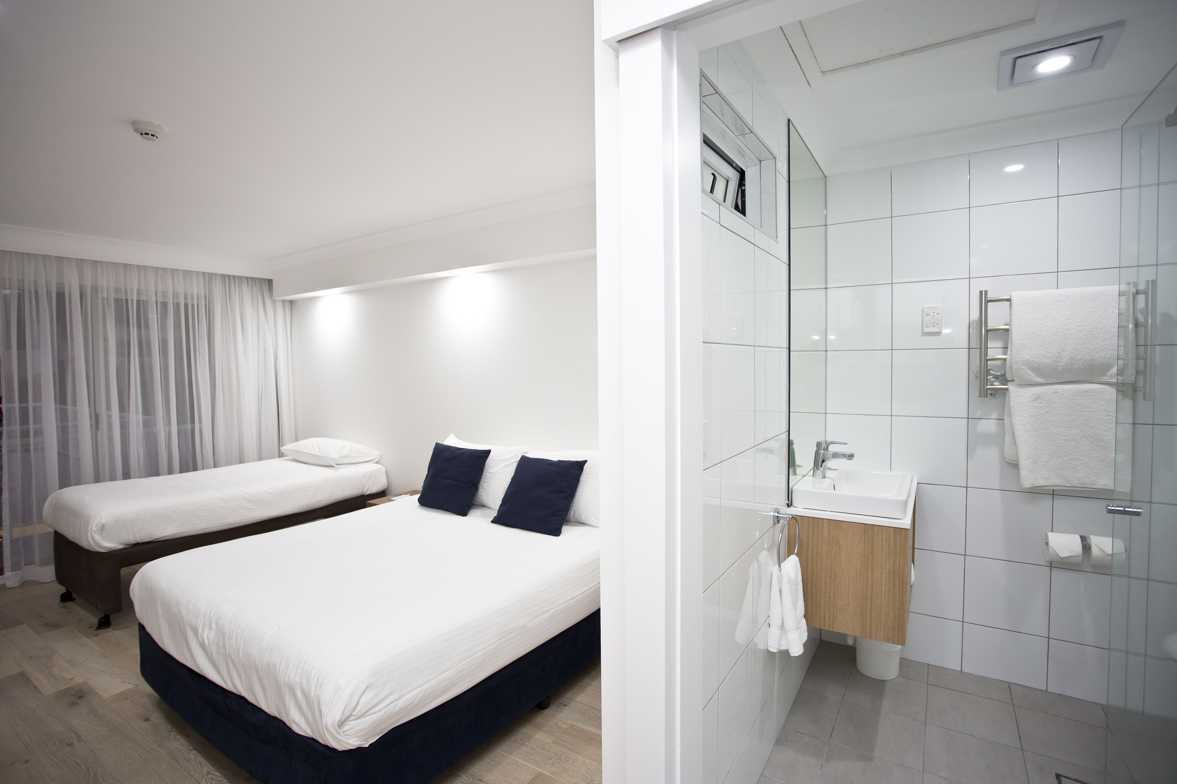 A hotel room with two beds, a bathroom with a glass shower, and a white color scheme.