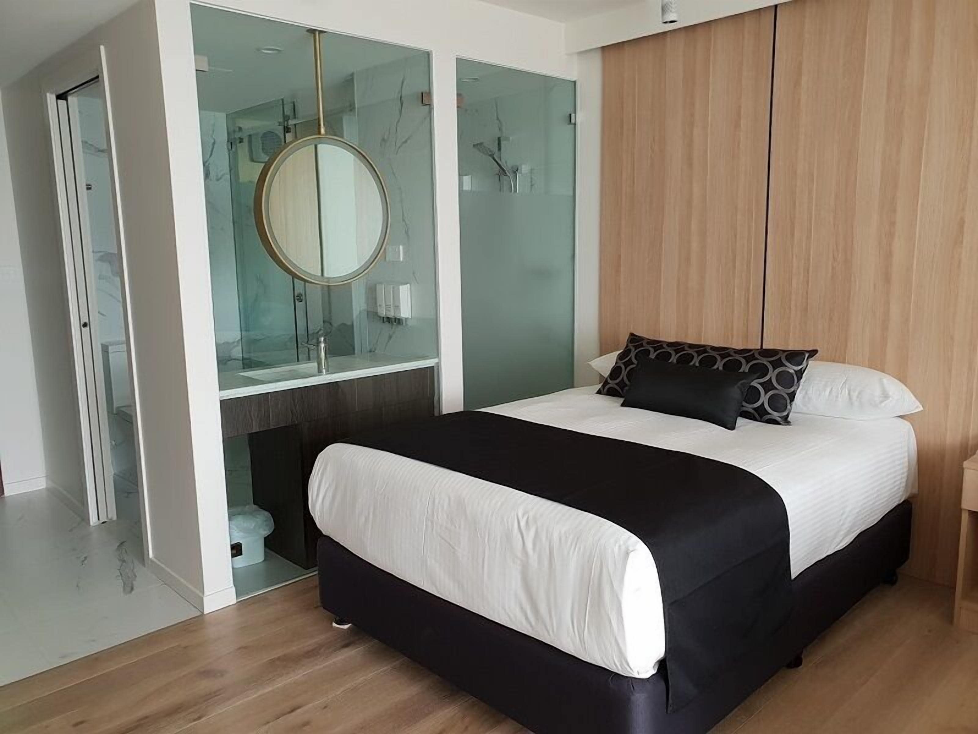 A modern bedroom with a large bed, a round mirror, and a wooden wardrobe.