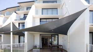 A modern multi-story building with balconies, large windows, and a covered outdoor area with a table and chairs. - Ocean Front at The Entrance (The Entrance)