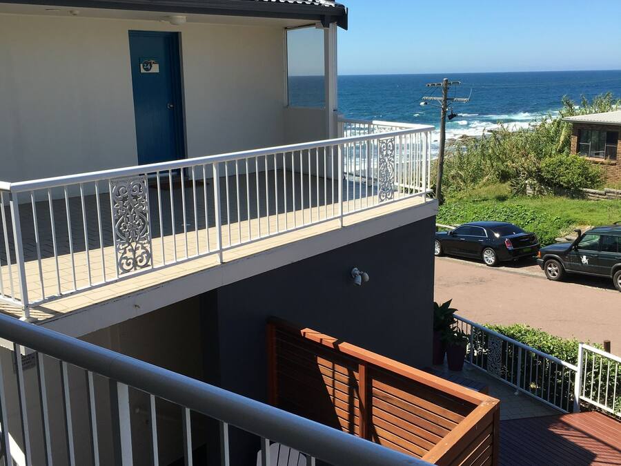 Un balcon avec vue sur l’océan, une porte bleue et une chaise blanche.