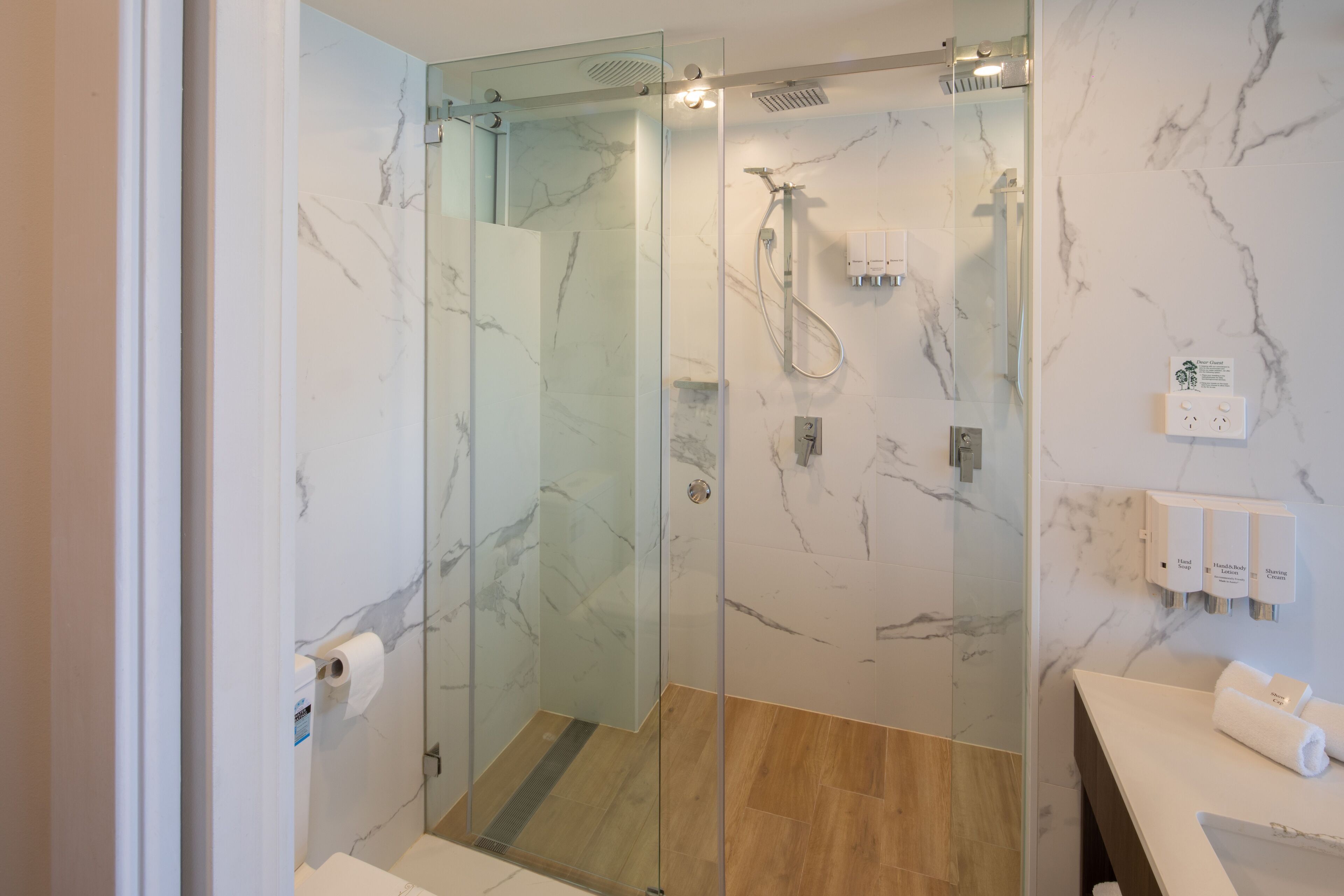 Een moderne badkamer met een douchecabine van glas, marmeren wanden en een houten vloer.