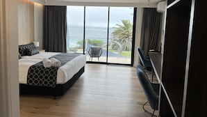 A modern hotel room with a large bed, a seating area with a view of the ocean, and a balcony with a curved railing. - Ocean Front at The Entrance (The Entrance)