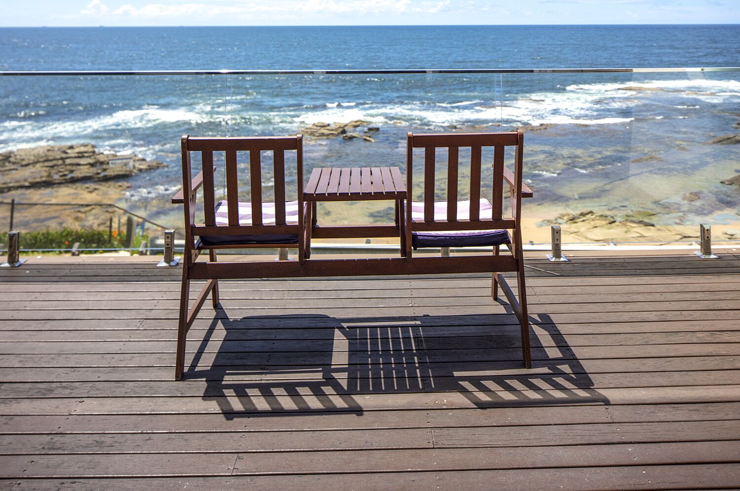 A wooden deck with a bench and table overlooking the ocean.