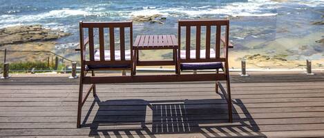 A wooden deck with a bench and table overlooking the ocean.