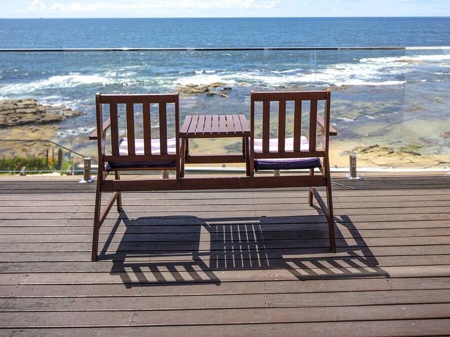 A wooden deck with a bench and table overlooking the ocean.