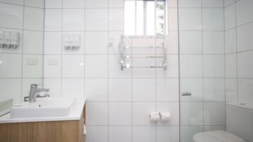 A modern bathroom with a white sink, mirror, and toilet. There is a window above the toilet, and a towel rack mounted on the wall.