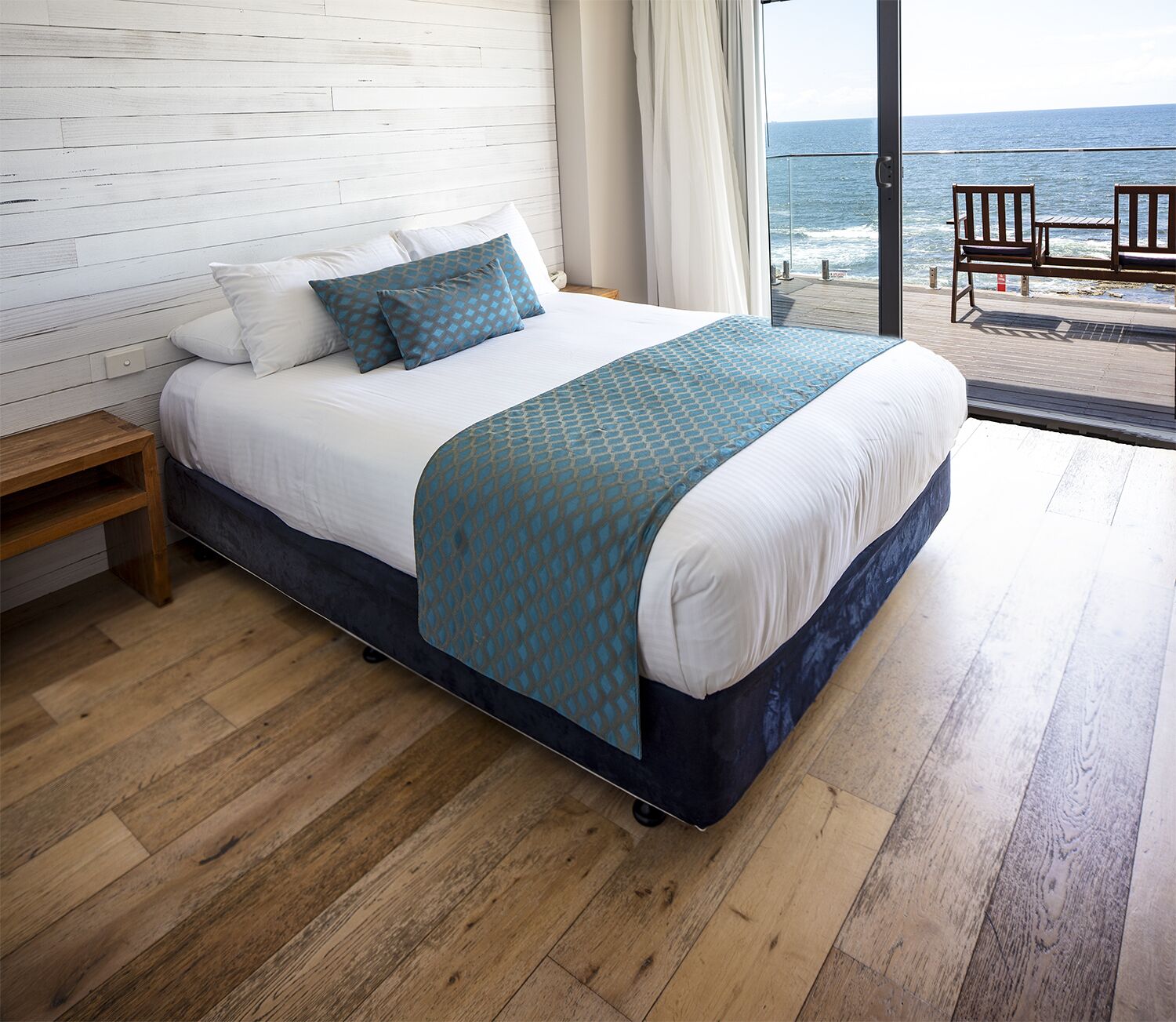 A bedroom with a bed, wooden floor, and a view of the ocean.