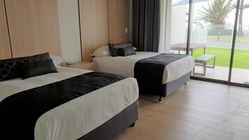 A hotel room with two beds, a large sliding glass door to a balcony, and a view of a fenced outdoor area.