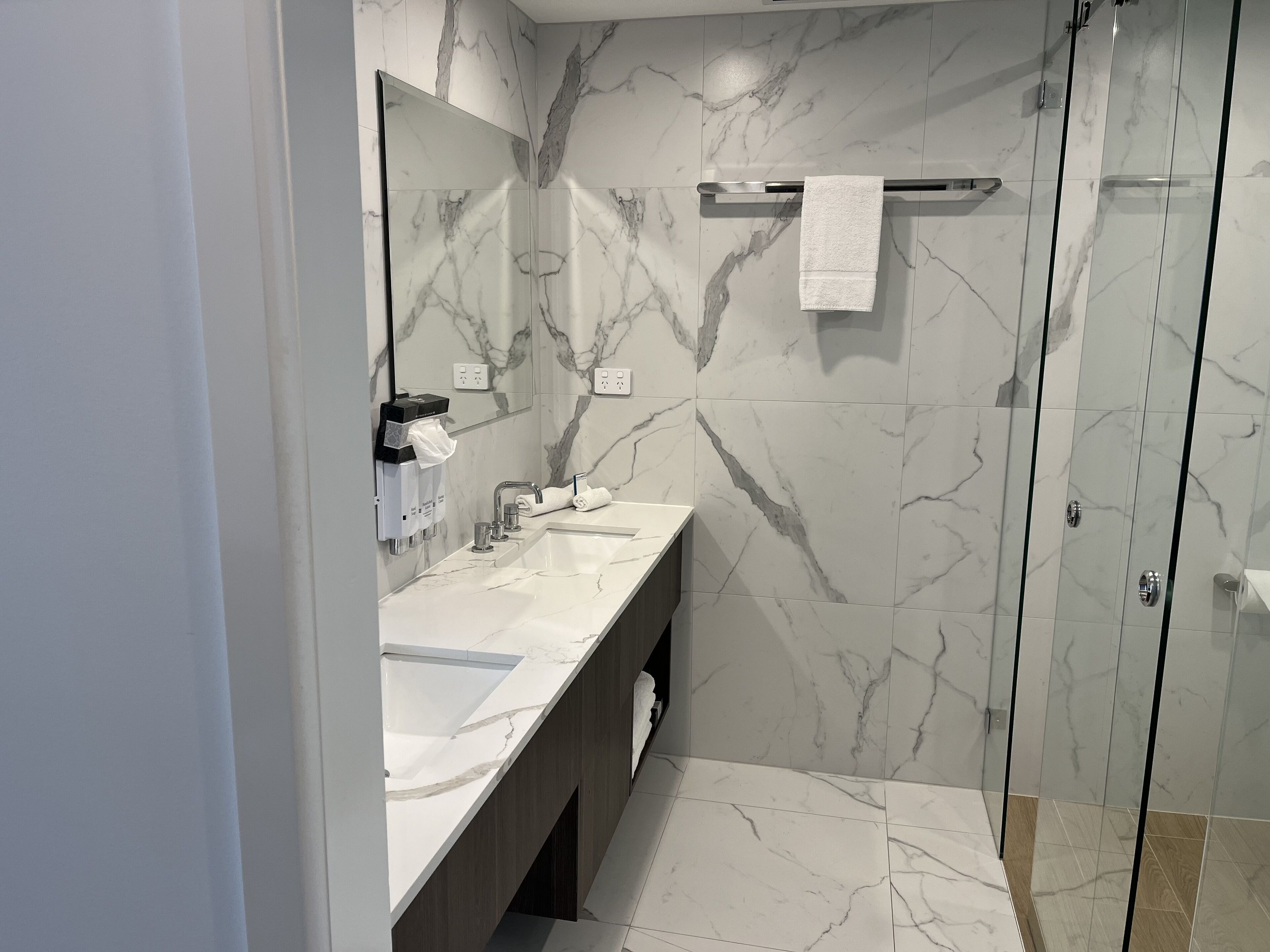 A modern bathroom with a marble backsplash, a glass shower enclosure, and a vanity with a sink and mirror.