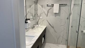 A modern bathroom with a marble backsplash, a glass shower enclosure, and a vanity with a sink and mirror.