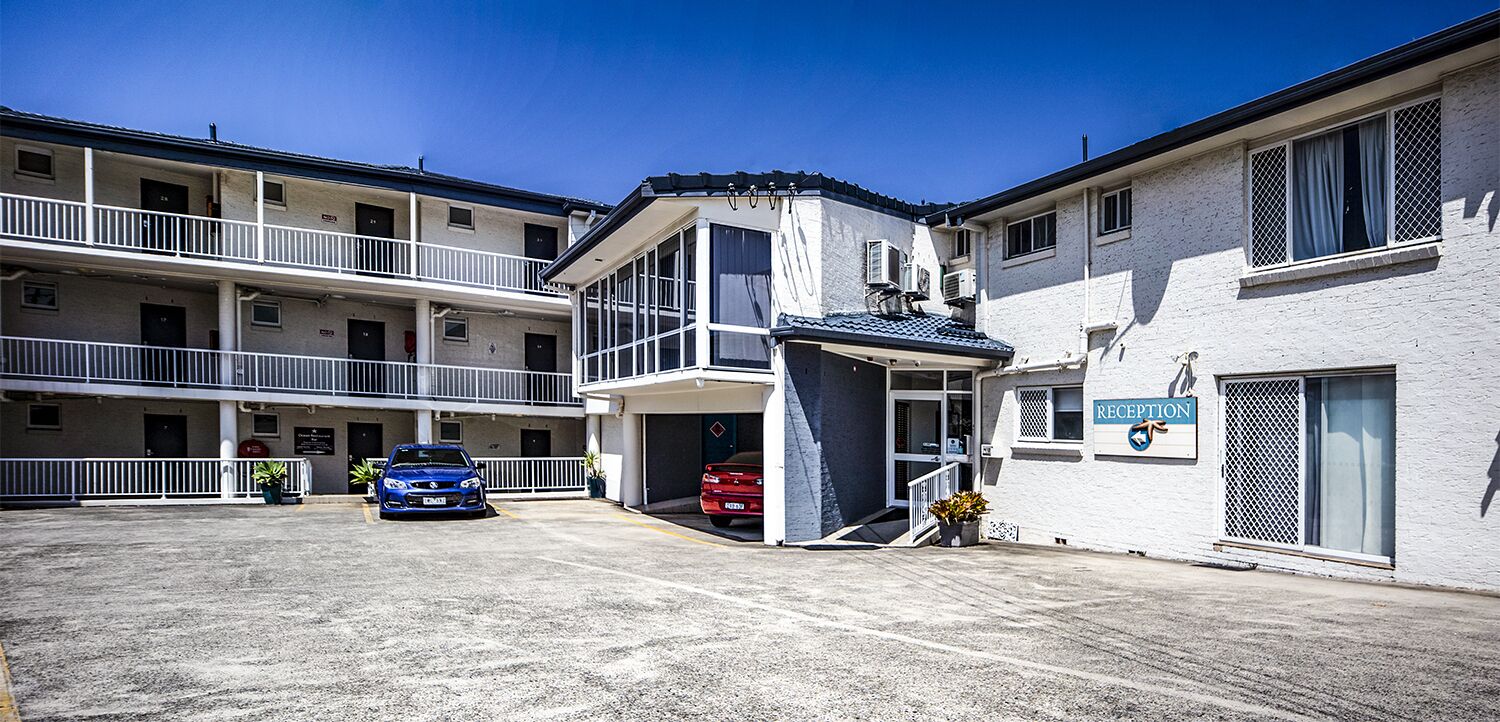 A multi-story hotel with a reception area, parking lot, and a balcony on the upper floor.