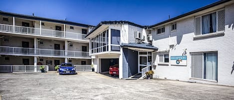 A multi-story hotel with a reception area, parking lot, and a balcony on the upper floor.