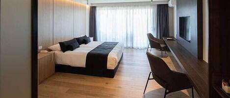 A modern hotel room with a large bed, a desk, and a TV mounted on the wall.