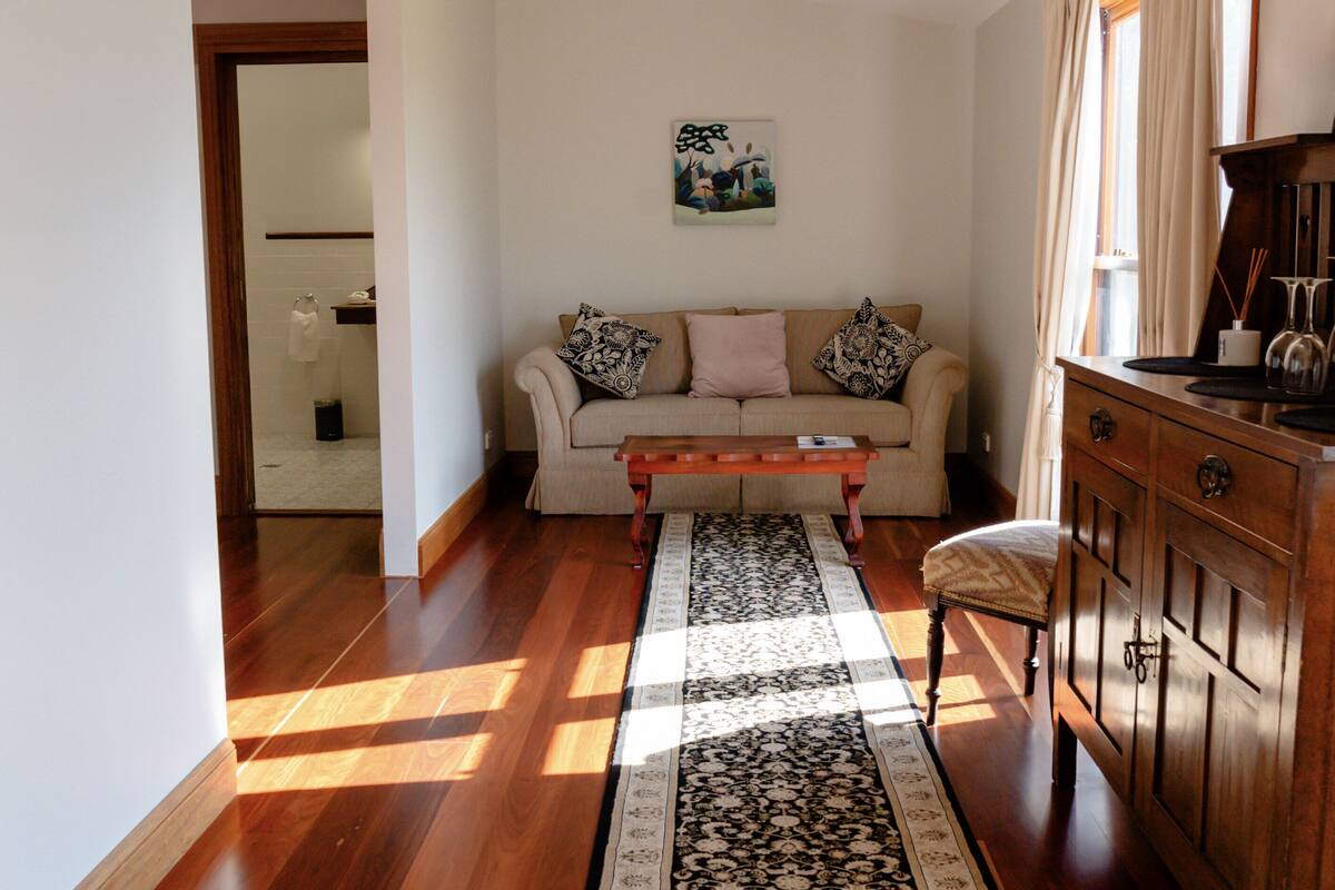 A living room with a wooden floor, a sofa with patterned cushions, a coffee table, and a wooden cabinet.