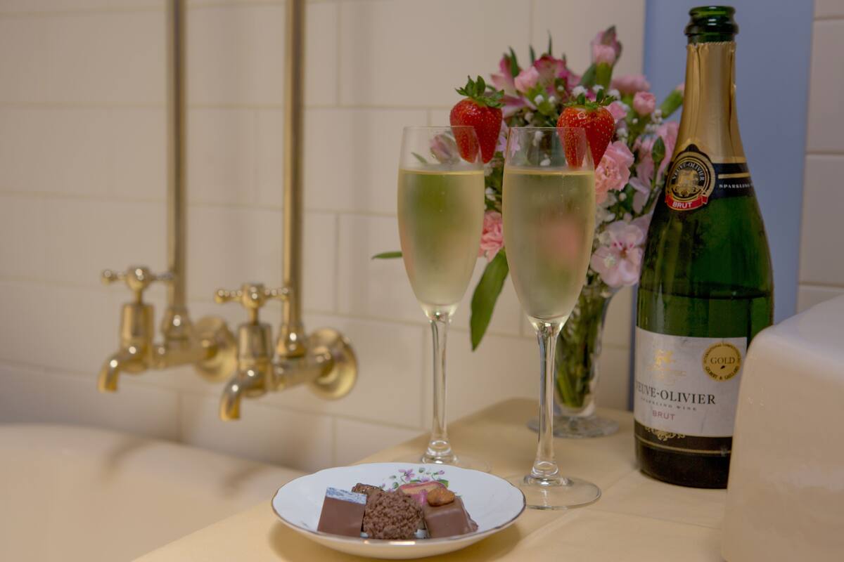 A champagne bottle, two glasses of champagne, a plate with chocolates, and a flower arrangement.