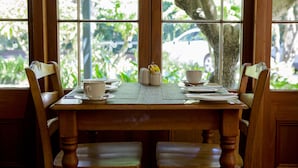 A dining table set with plates, cups, and a salt shaker, positioned in front of a window with a view of greenery and a car outside.