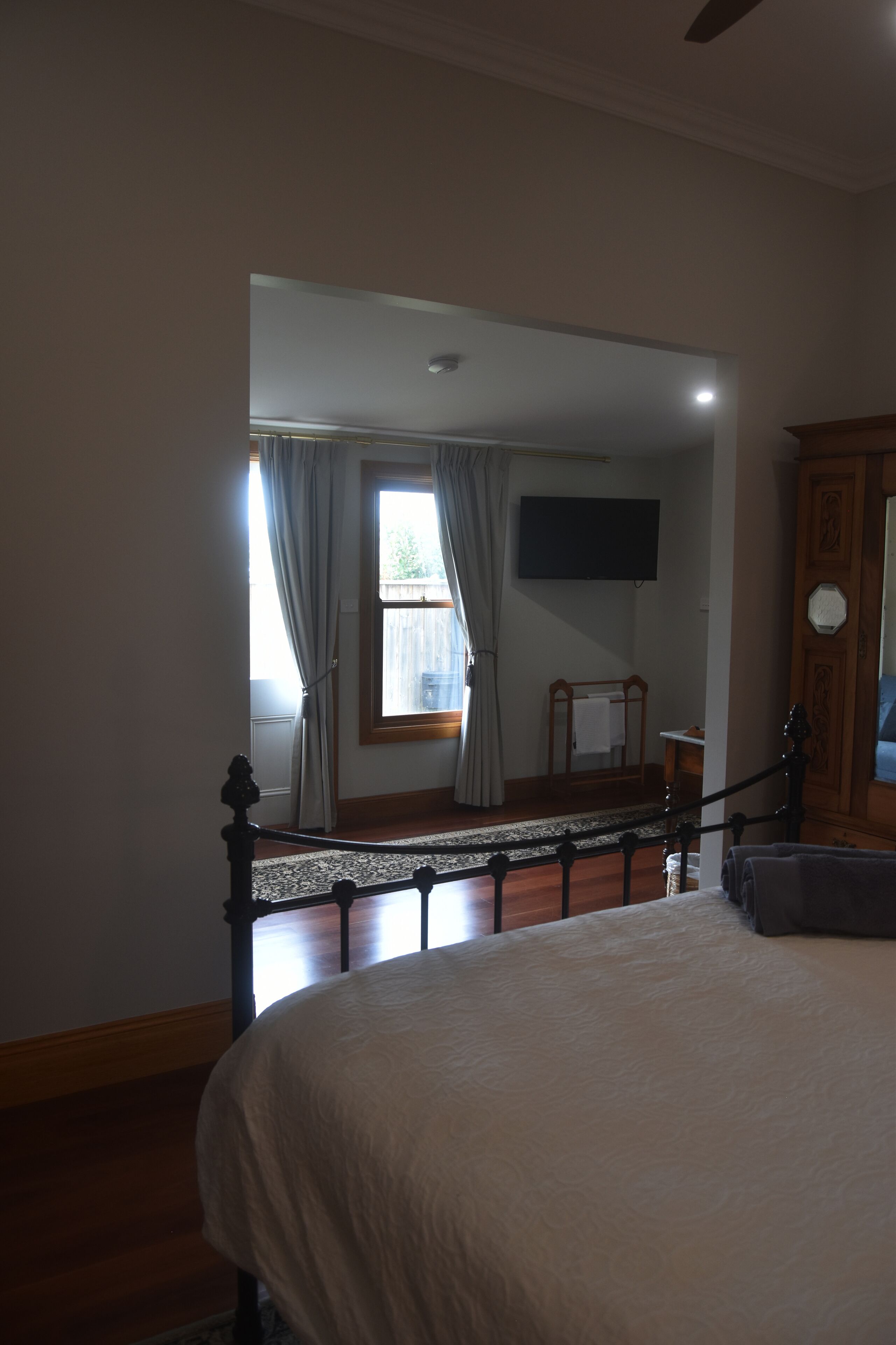 A bedroom with a large bed, a wooden headboard, a flat-screen TV mounted on the wall, and a window with curtains.