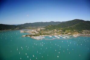 Une vue aérienne d’une zone côtière avec de nombreux bateaux, un port de plaisance et une ville avec des bâtiments et de la végétation.