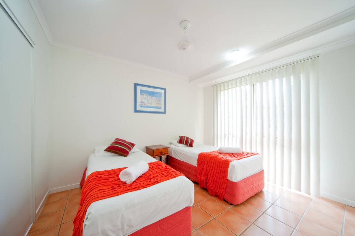 Una habitación de hotel con dos camas, una mesita y una ventana con persianas.