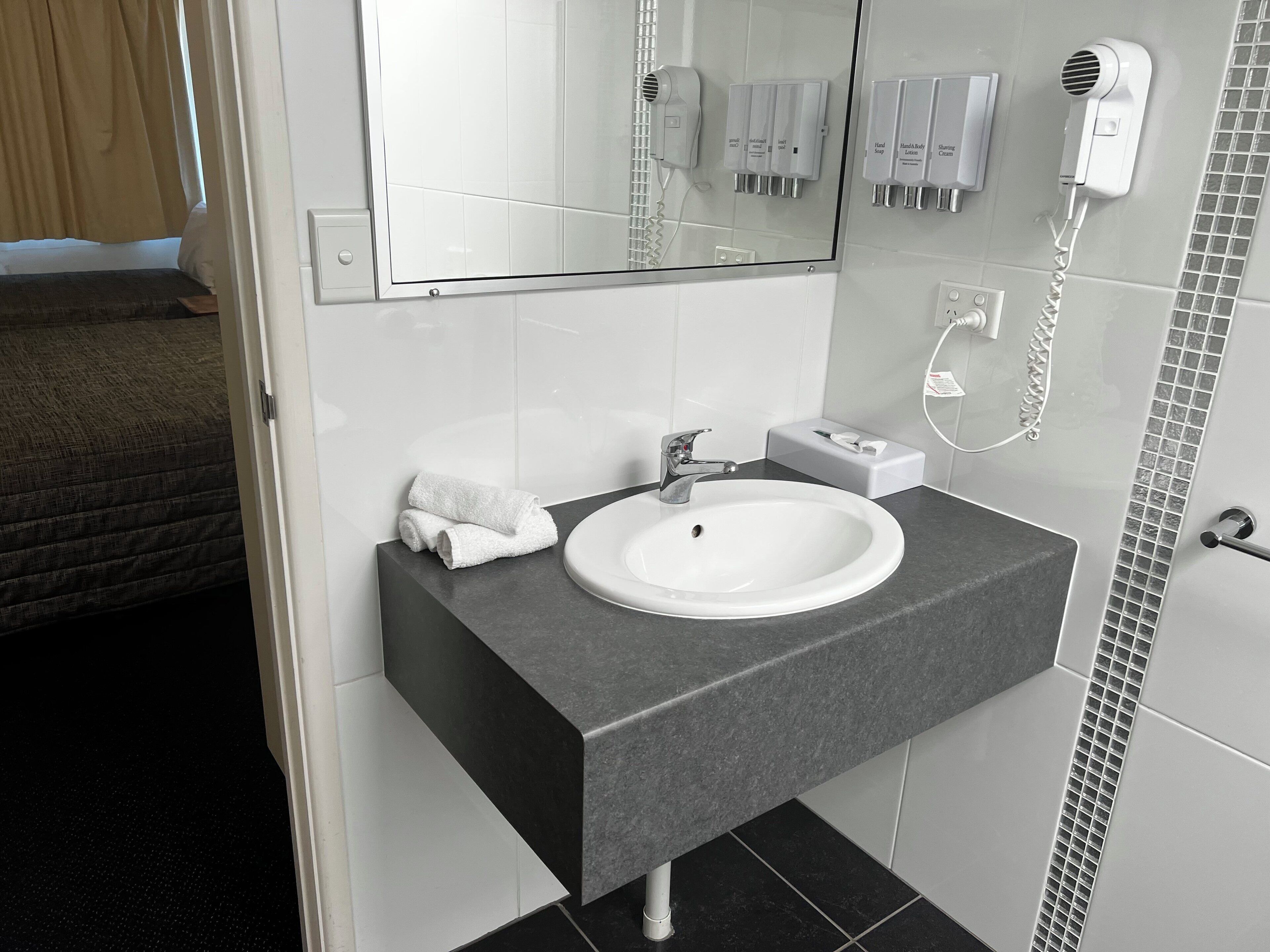 Ein modernes Badezimmer mit einem weißen Waschbecken, einer dunklen Arbeitsplatte und einem Spiegel darüber.