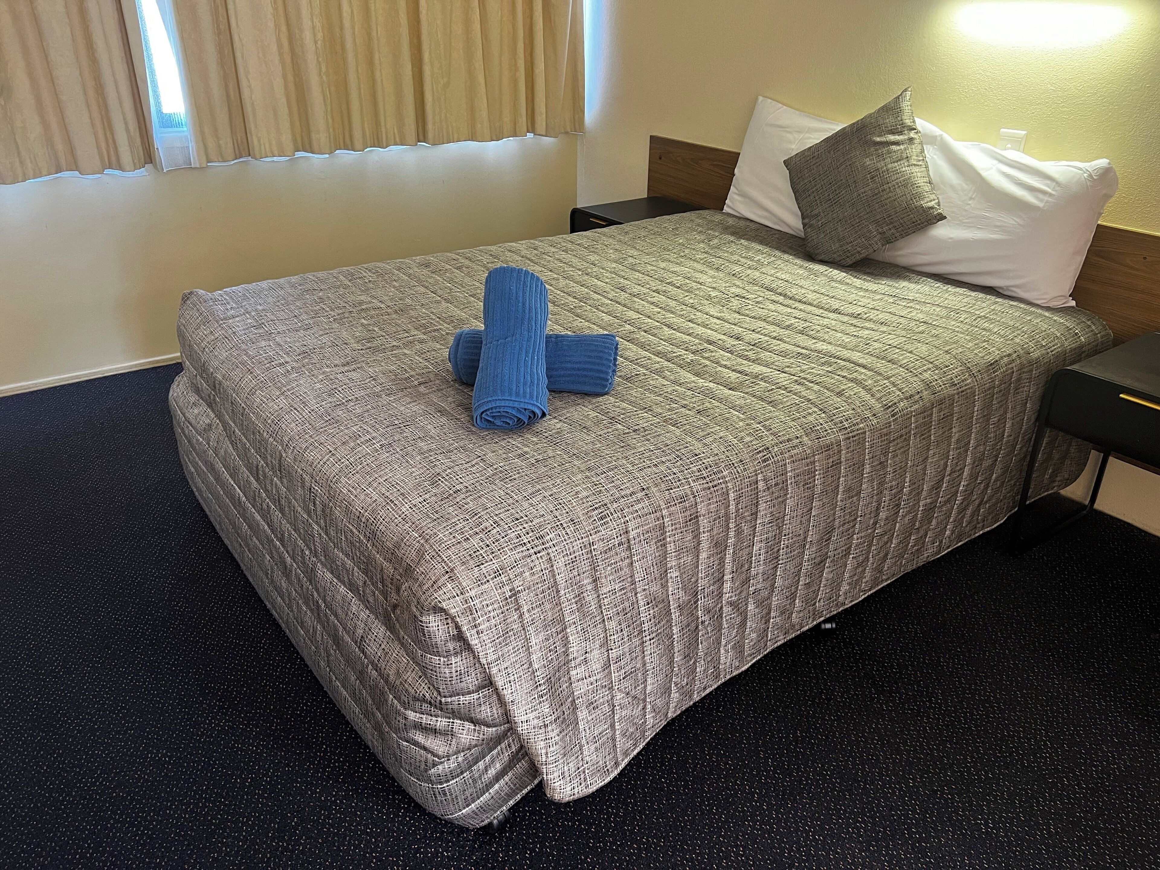 A neatly made bed with a textured blanket, two pillows, and a rolled-up towel on the bed.
