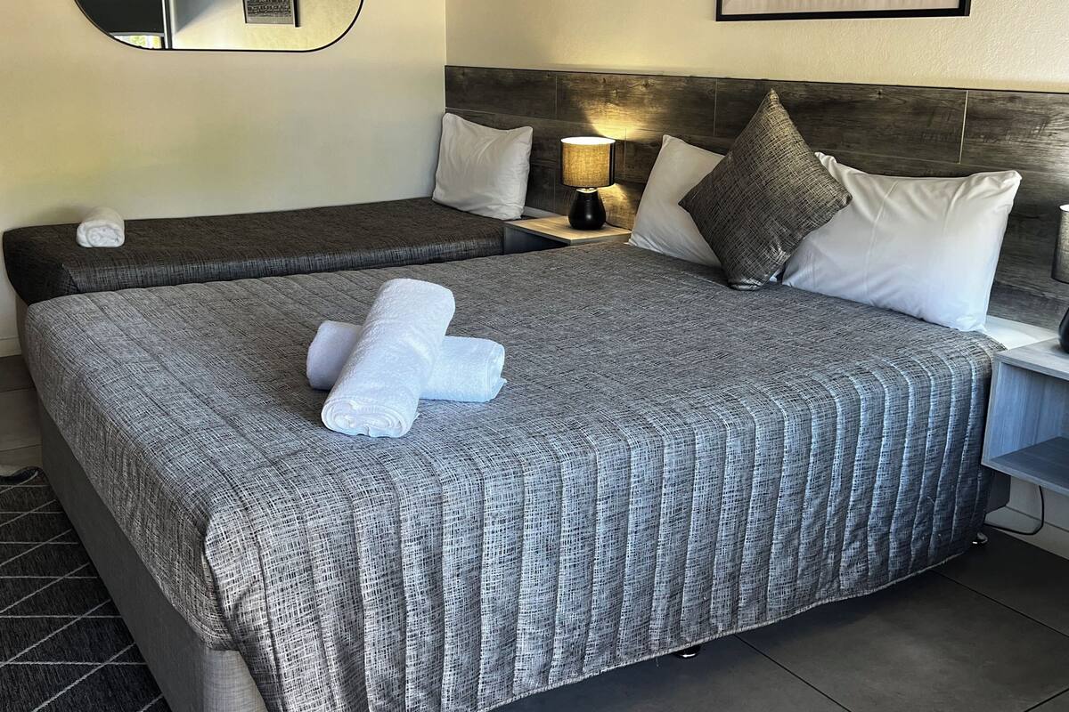 Habitación de hotel con dos camas, una mesita de noche con lámpara, un cuadro en la pared y una toalla sobre la cama.
