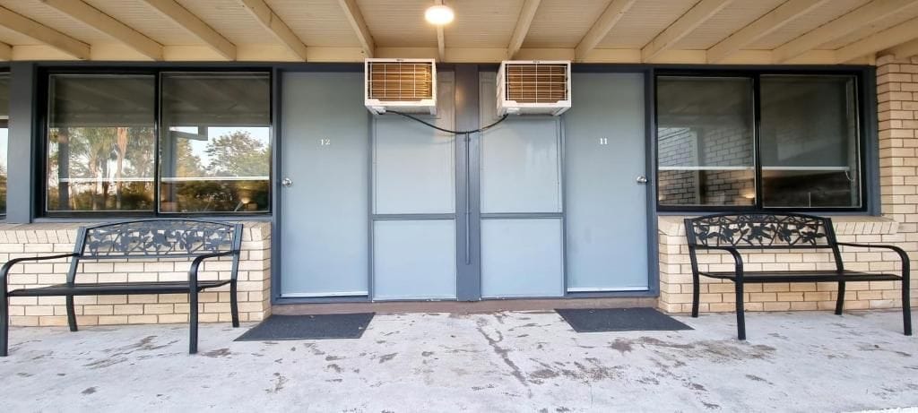Entrada de un edificio con dos unidades de aire acondicionado, un conjunto de puertas dobles y dos bancos afuera.