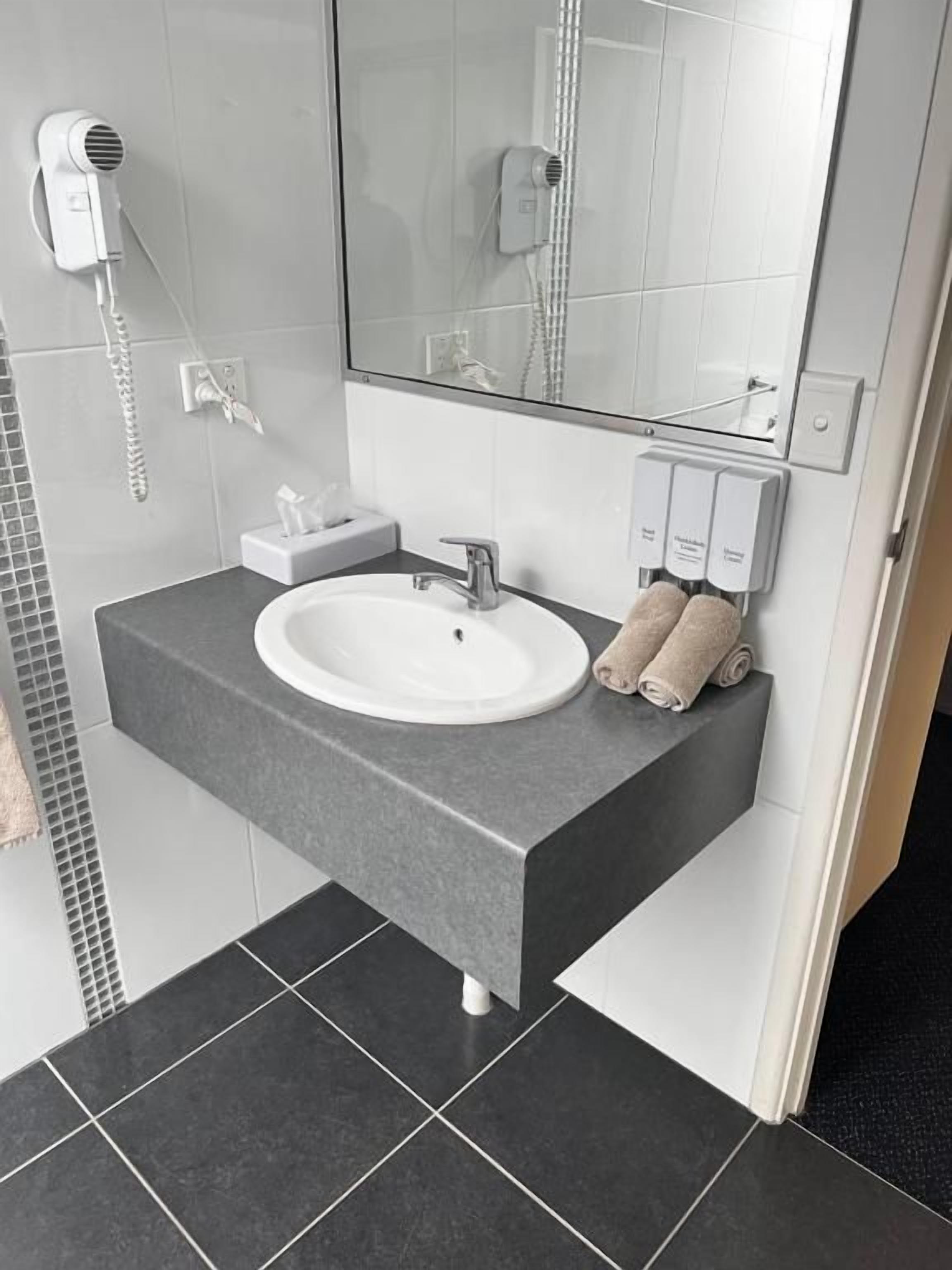 A bathroom with a white sink, a mirror, a hairdryer, and a towel rack.
