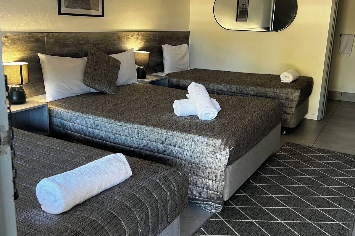 Habitación de hotel con dos camas, cabeceras, lámparas de noche, un espejo y toallas sobre las camas.