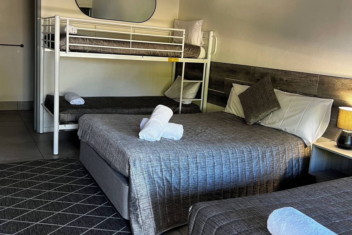 Habitación de hotel con literas, una cama individual, una mesita de noche con lámpara y un espejo en la pared.