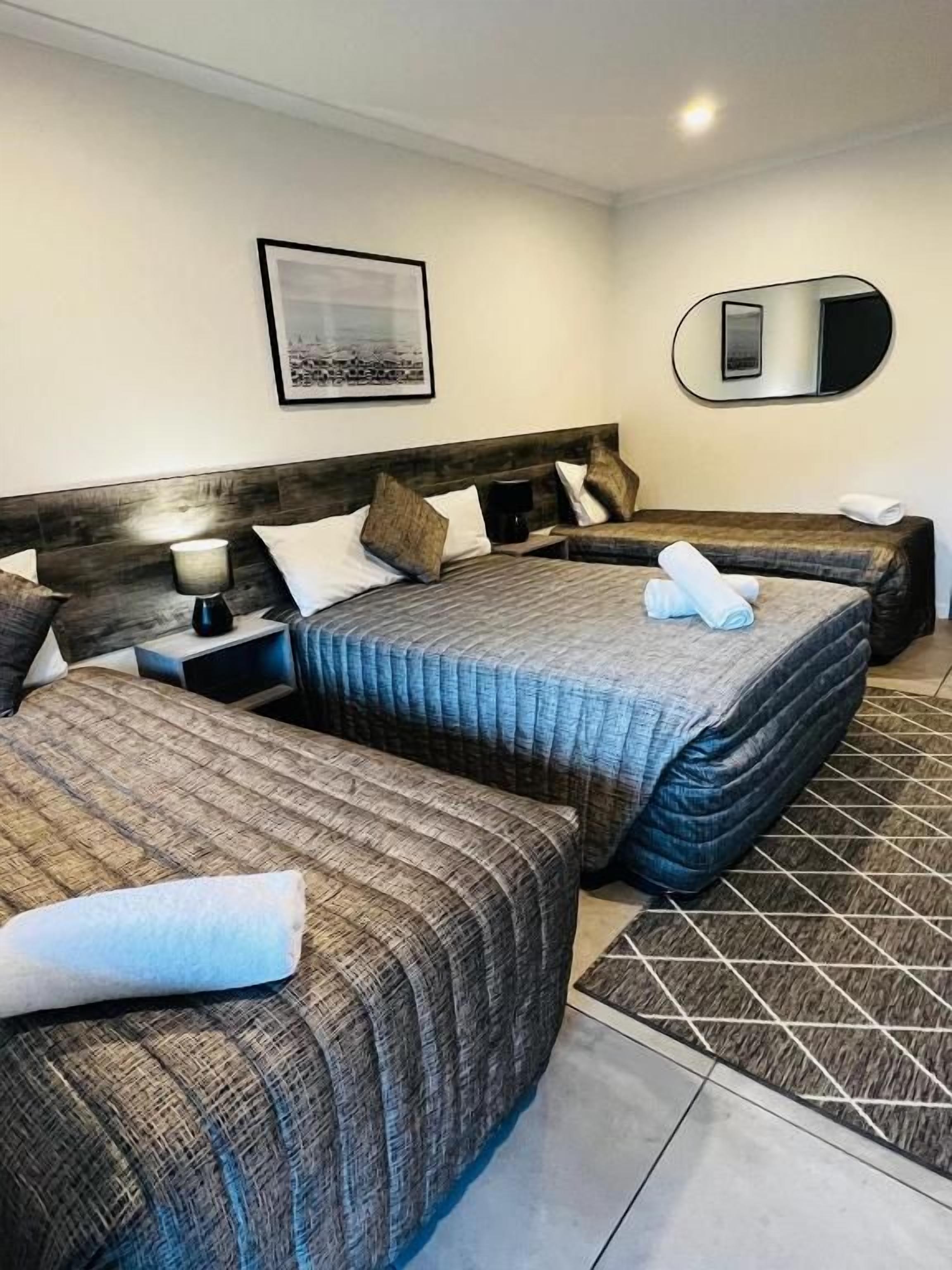 A hotel room with two beds, a nightstand, a lamp, a mirror, and a framed picture on the wall.