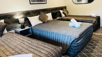 A hotel room with two beds, a nightstand, a lamp, a mirror, and a framed picture on the wall.