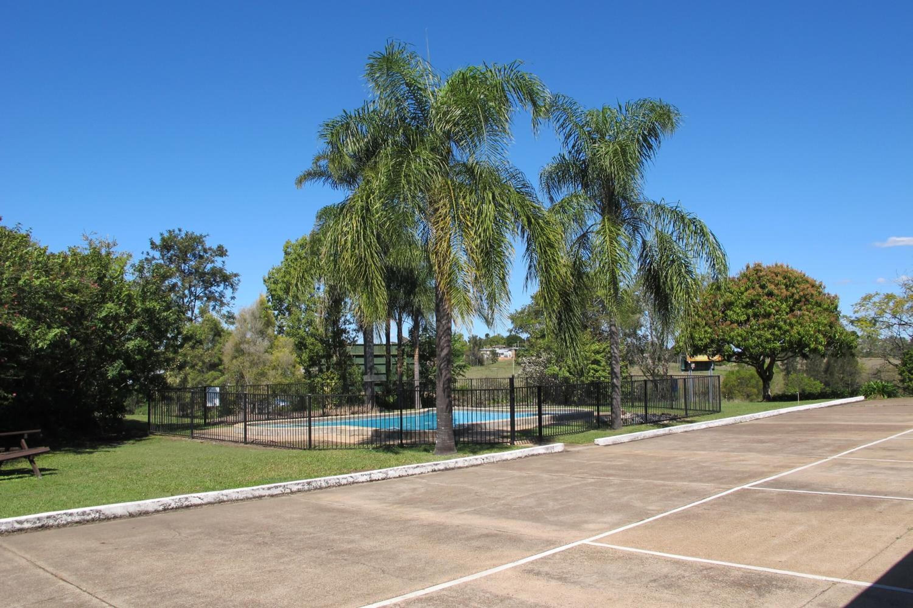 Un parking avec une piscine, entouré de palmiers et d’une clôture.