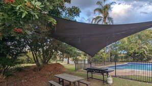 Un área de picnic con una mesa y bancos, una parrilla y una piscina al fondo.