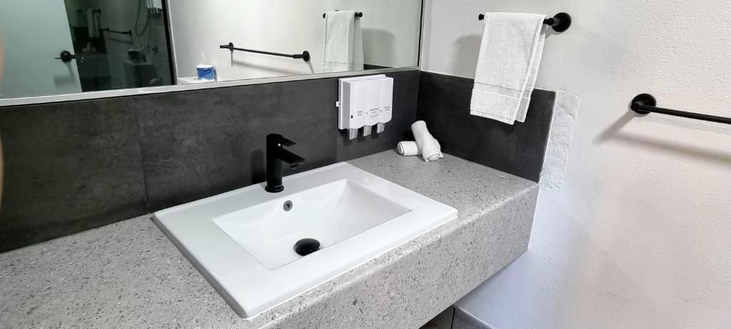 Un baño con lavamanos blanco, espejo, dispensador de toallas y perchero.