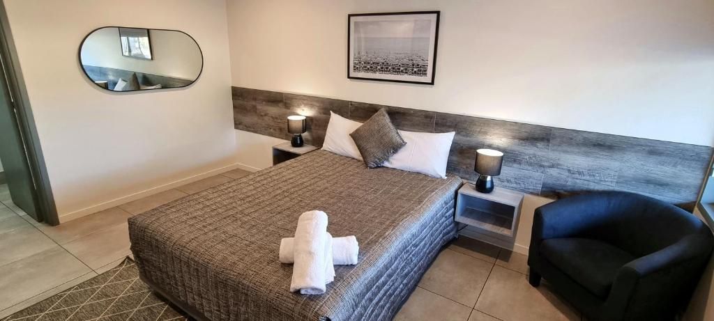 Habitación de hotel con cama, dos mesitas de noche, una silla, un espejo y un cuadro en la pared.